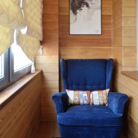 Темно-синее кресло на лоджии с деревянной обшивкой