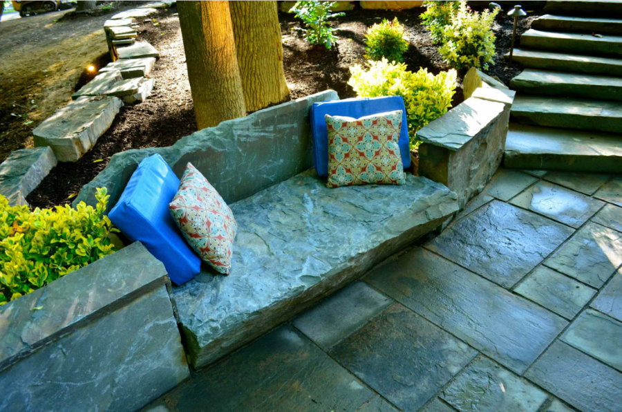 Мягкие подушки на каменной скамейке в саду